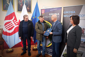 Podpisujący umowę na tle flag i banerów Gminy Włoszakowice
